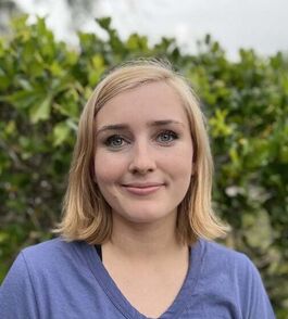 A headshot of Alyssa, a massage therapist, with green foliage in the background