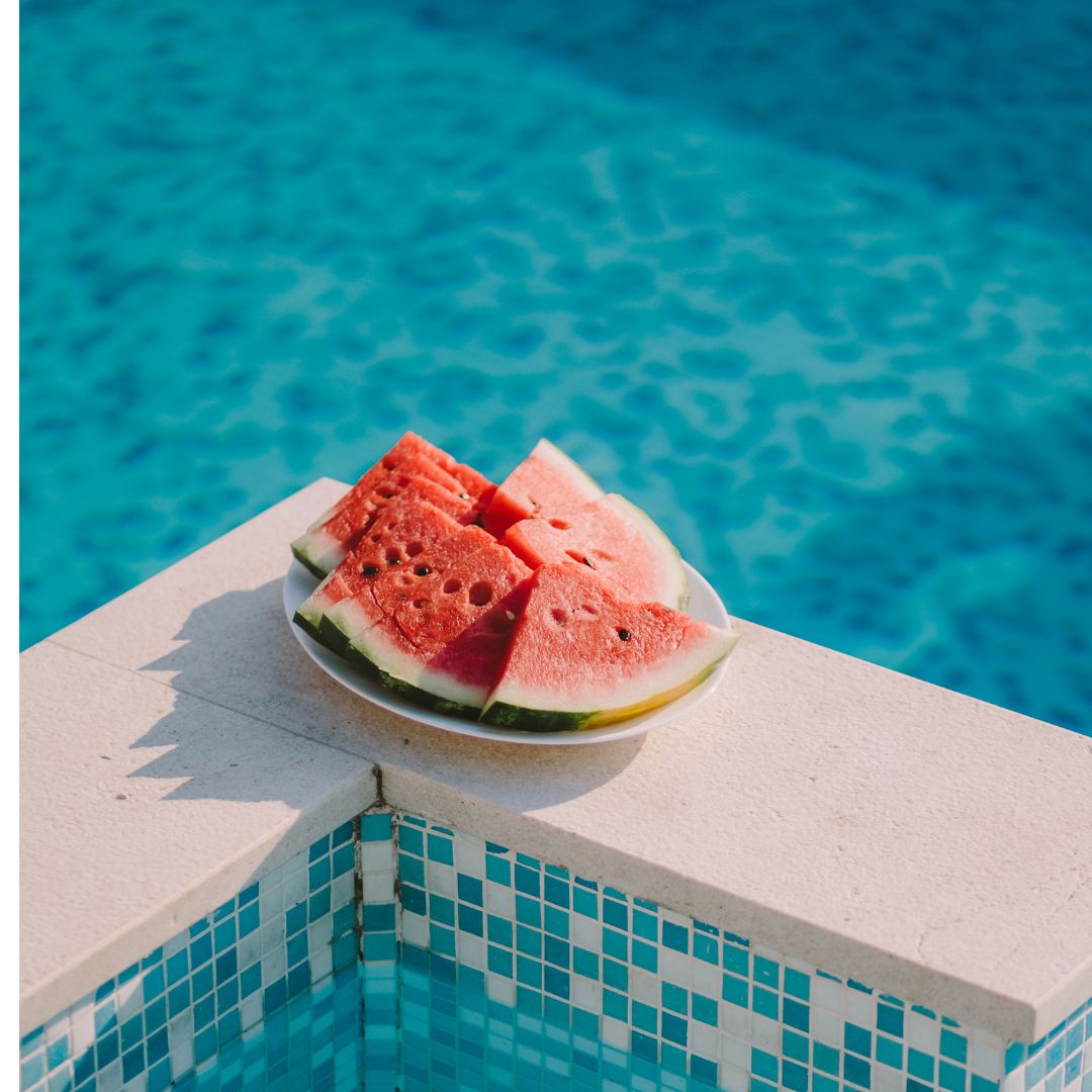 A plate full of cut watermelon sits by a pool with blue water