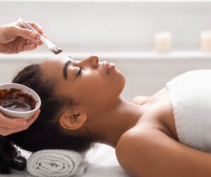 A young woman lying face up receiving a facial in a spa setting