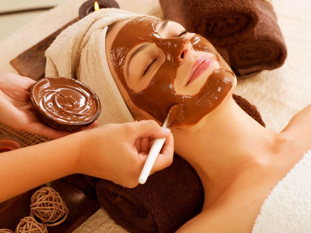 A woman receives a chocolate facial, which is applied with a brush by an esthetician 