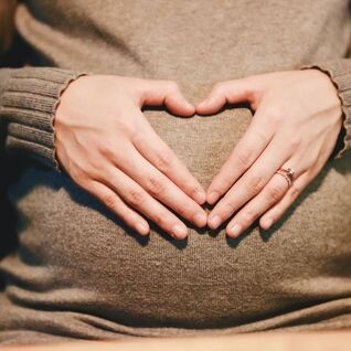 A pregnant belly with two hands in the shape of a heart