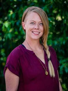 A headshot of Heather Lukens, a massage therapist, with green foliage in the background