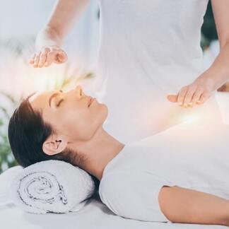 A woman relaxes during a reiki treatment, as hands are placed over her head and chest