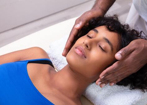 A woman relaxes during a reiki treatment while hands are placed on either side of her head