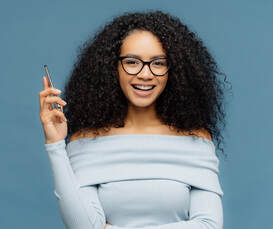 A teenage young woman with curly hair and glasses looks ahead and smiles