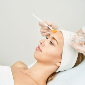 A woman in a spa setting received a facial, with a chemical peel being brushed on her face