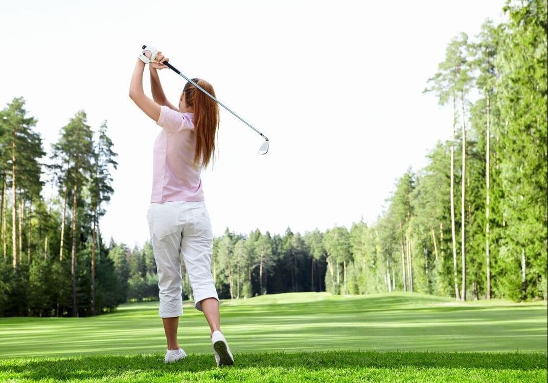 A woman plays golf on a wooded golf course