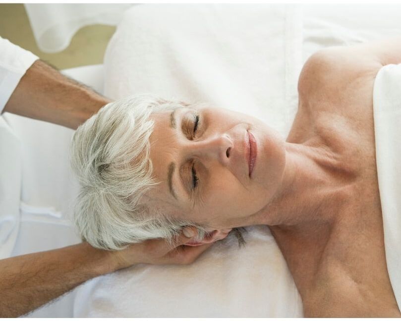 An older woman with short white hair receives a massage and looks peaceful